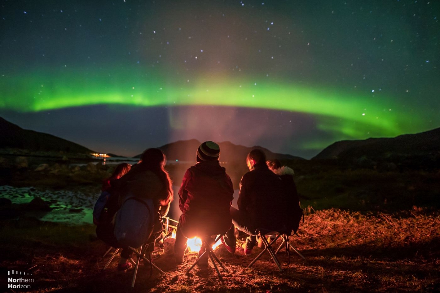 People gathered around a bonfire looking at the Northern Lights