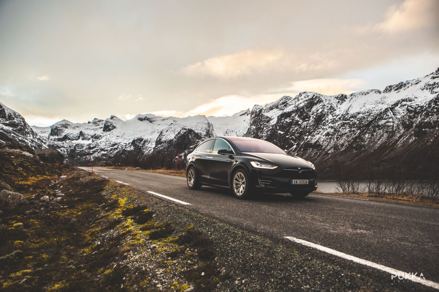 A black Tesla driving on a road with snowy hills in the background