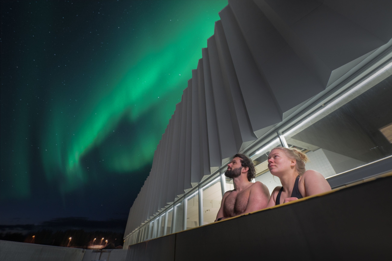 Man and woman in a pool under the Northern Light sky