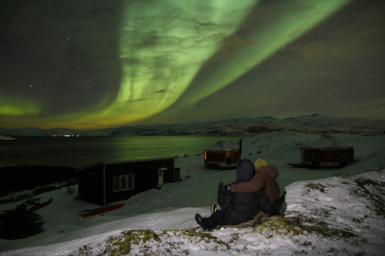 Two people sitting on a hill watching the Northern Lights
