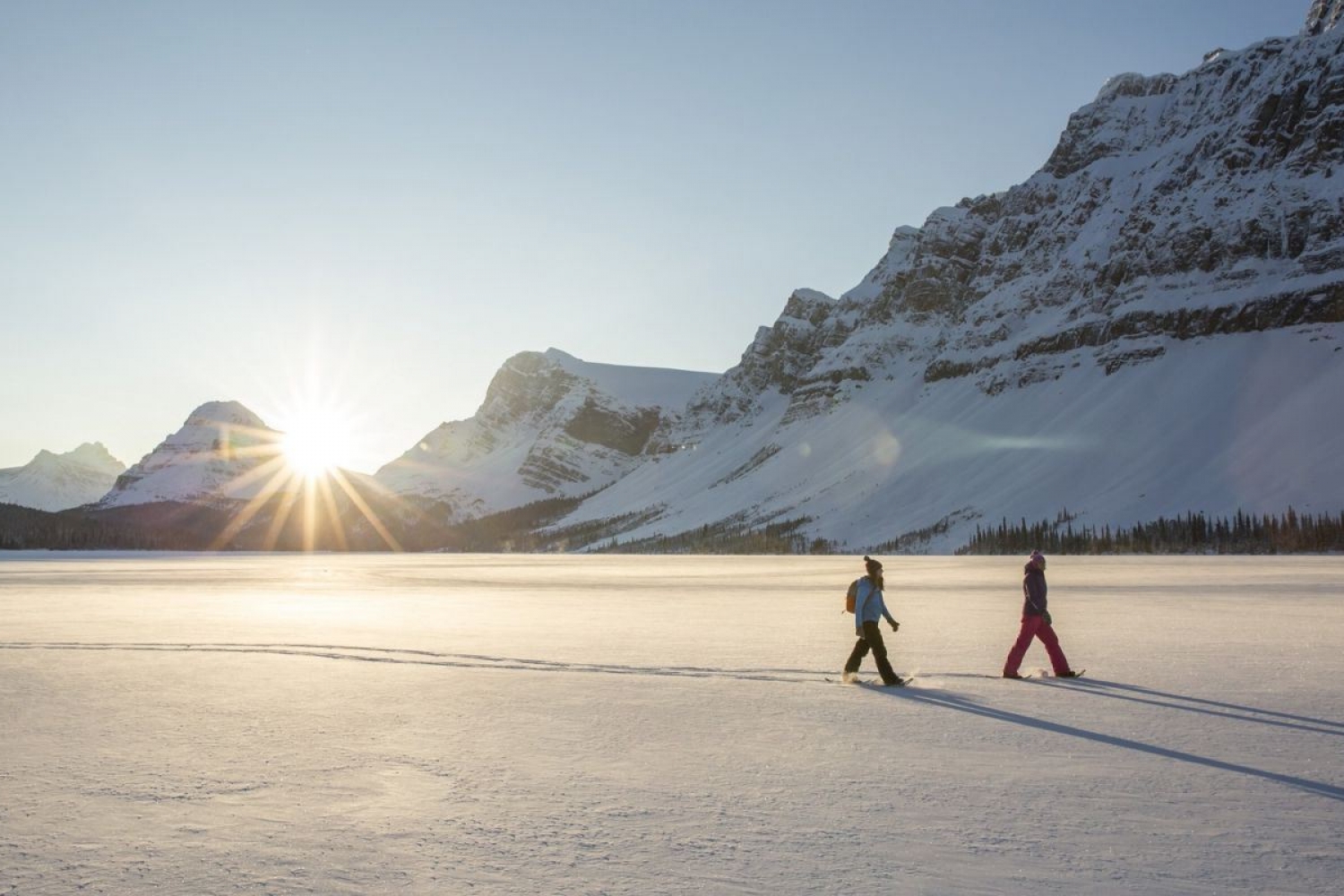 To personer går på truger på et solfylt og snødekt landskap