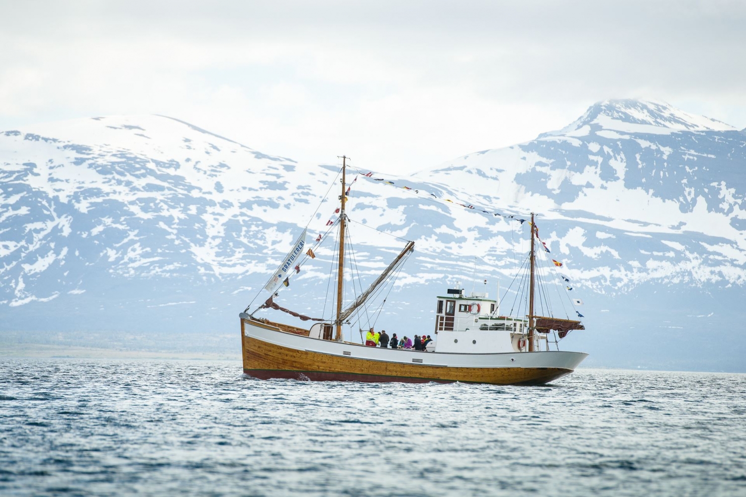 The wooden boat Hermes II out on the sea with snowy mountains in the background