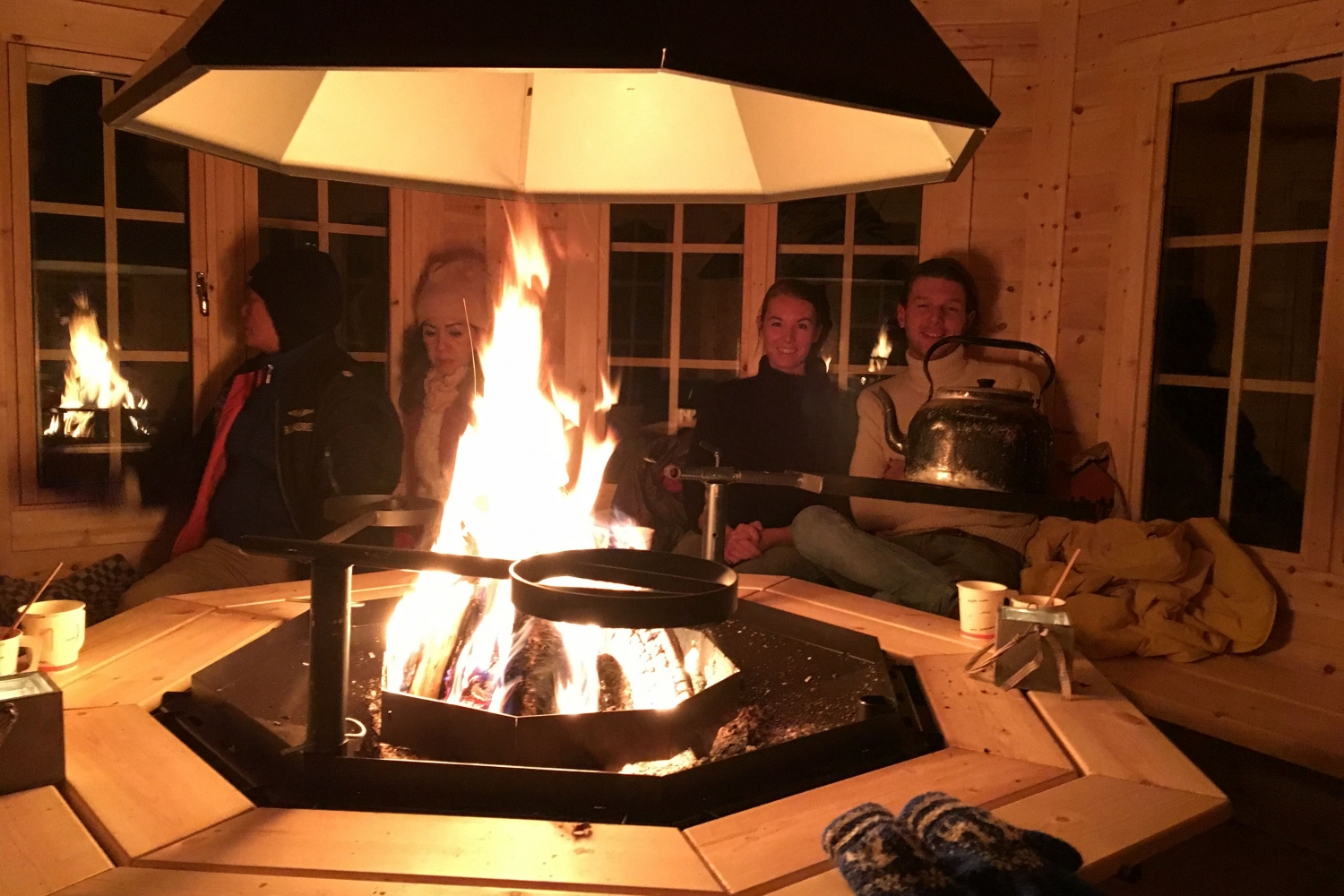 Persons sitting inside a hut with a bonfire in the middle