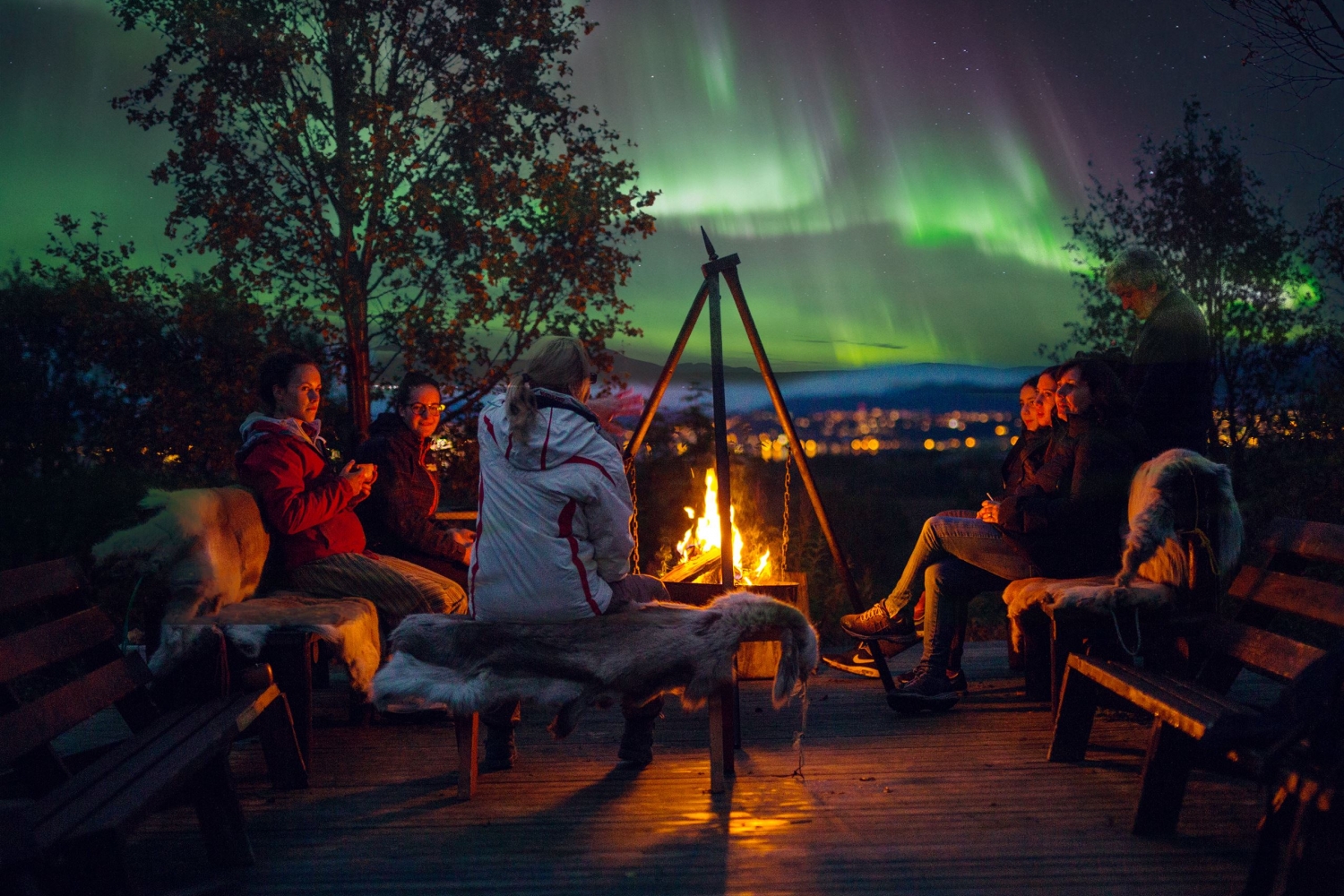 Guests gathered around a bonfire with Northern Lights in the background