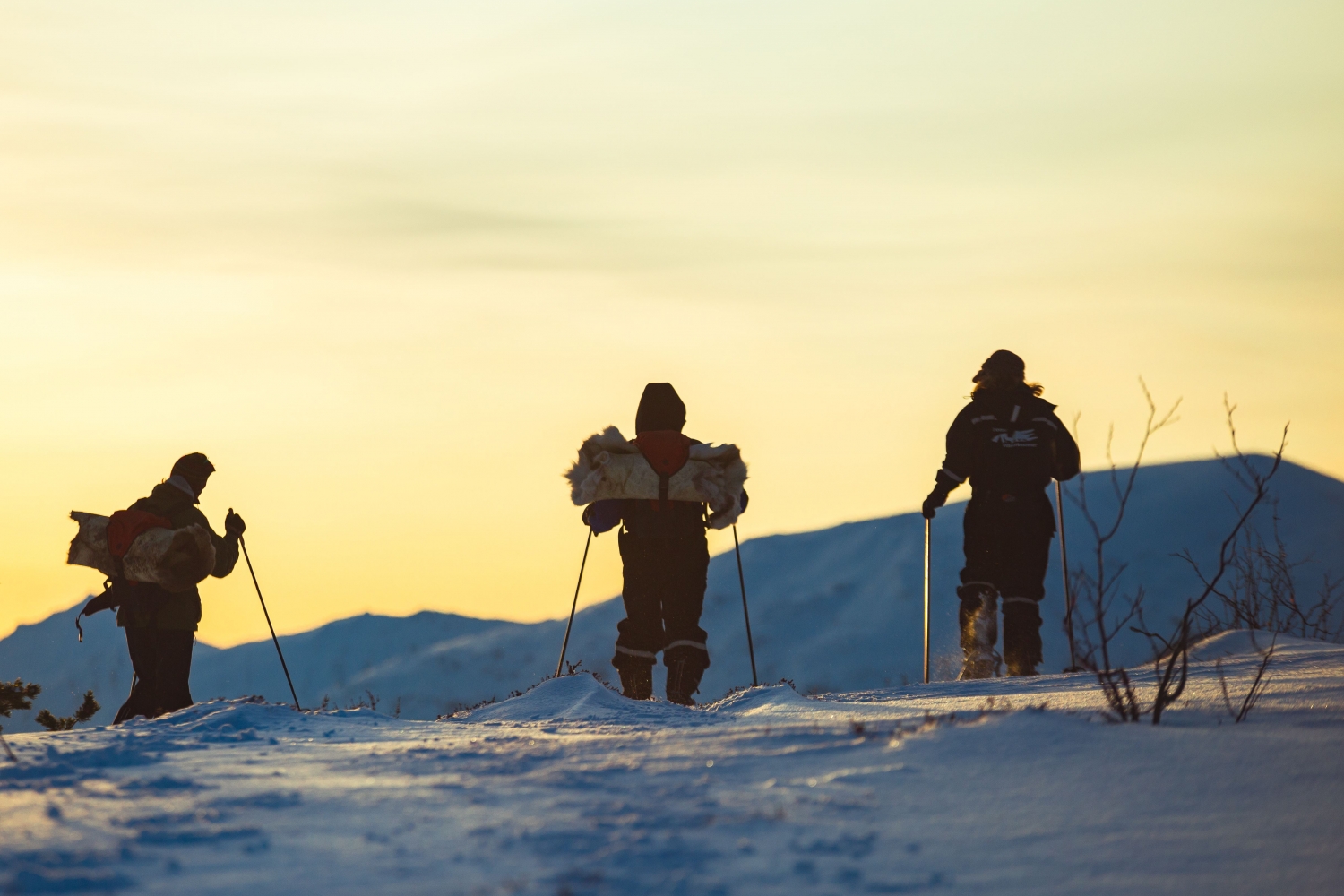 Three persons on snowshoes admiring the yellow coloured sky