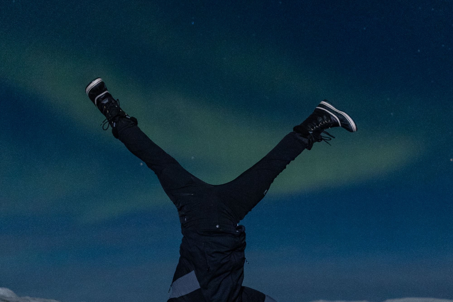 man doing somersault on the rocks under northern lights