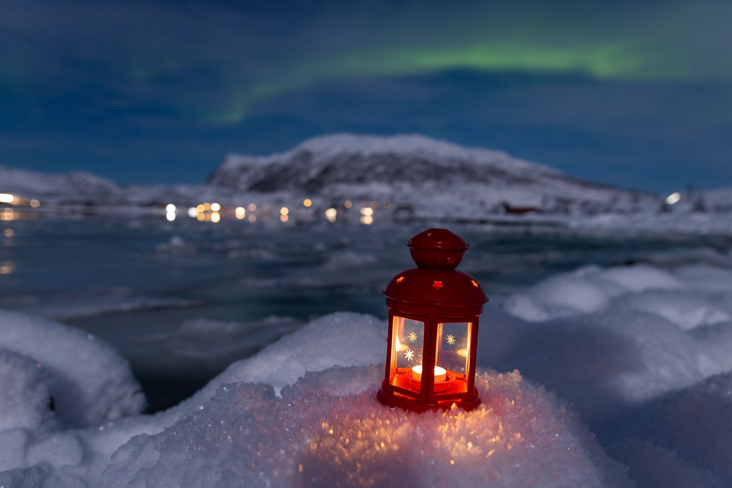 candle on snow under northern lights