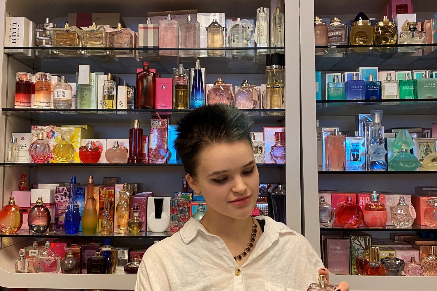 Person trying a perfume with the perfume shelf in the background