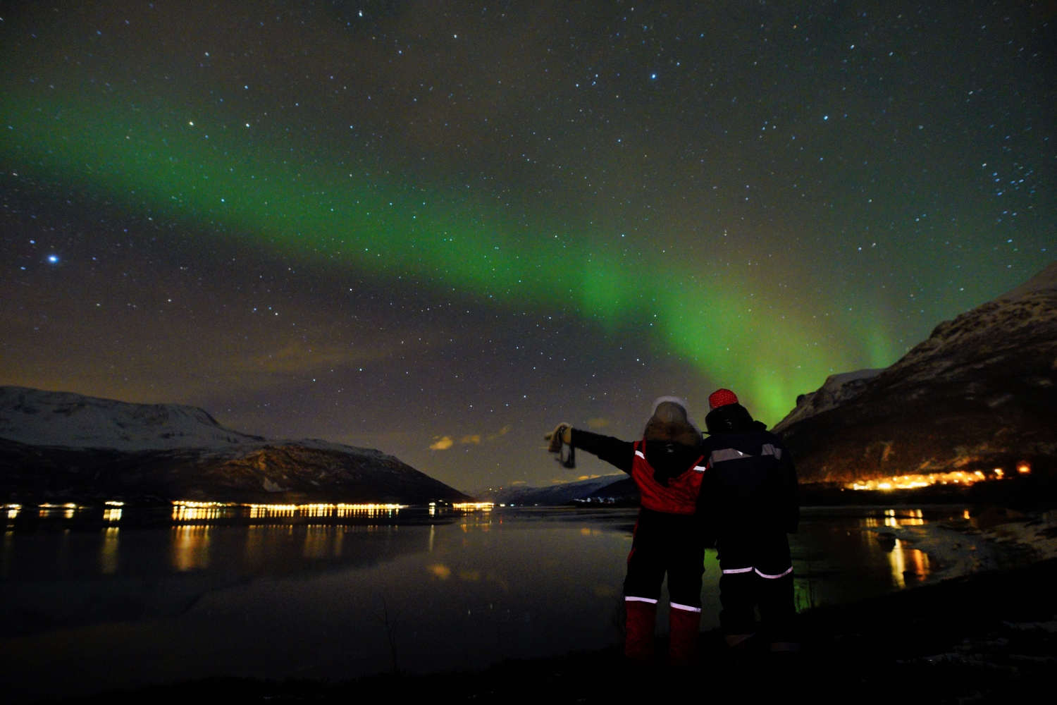 two people enjoying the northern lights by the fjord