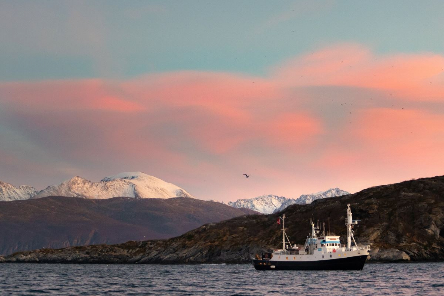 the boat in beautiful surroundings with mountains, sea and pink clouds