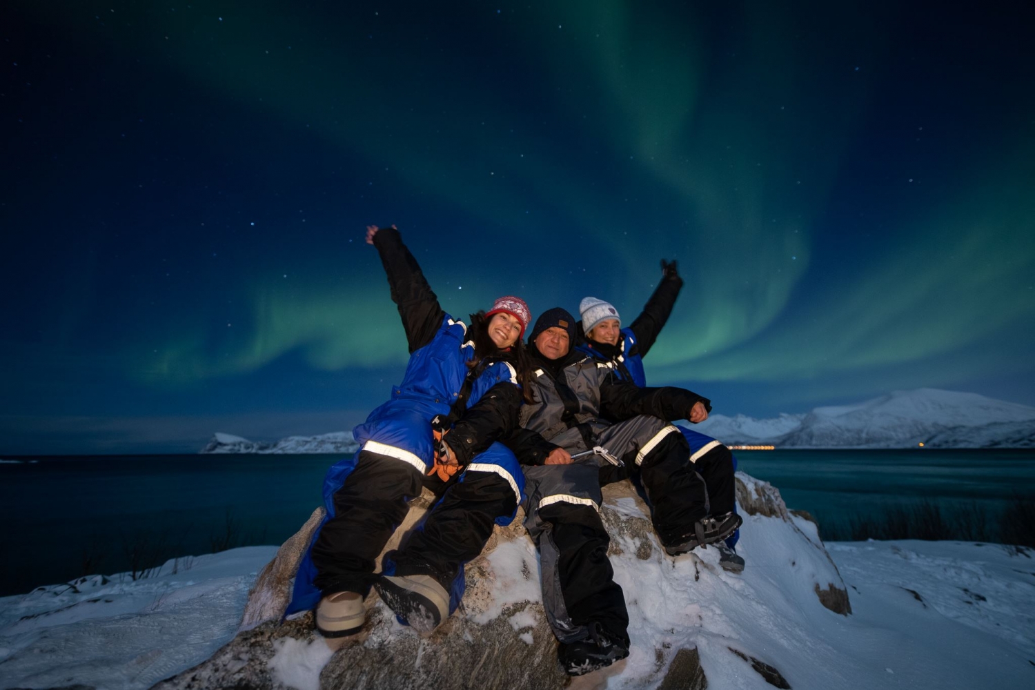 three people under a sky full of northern lights