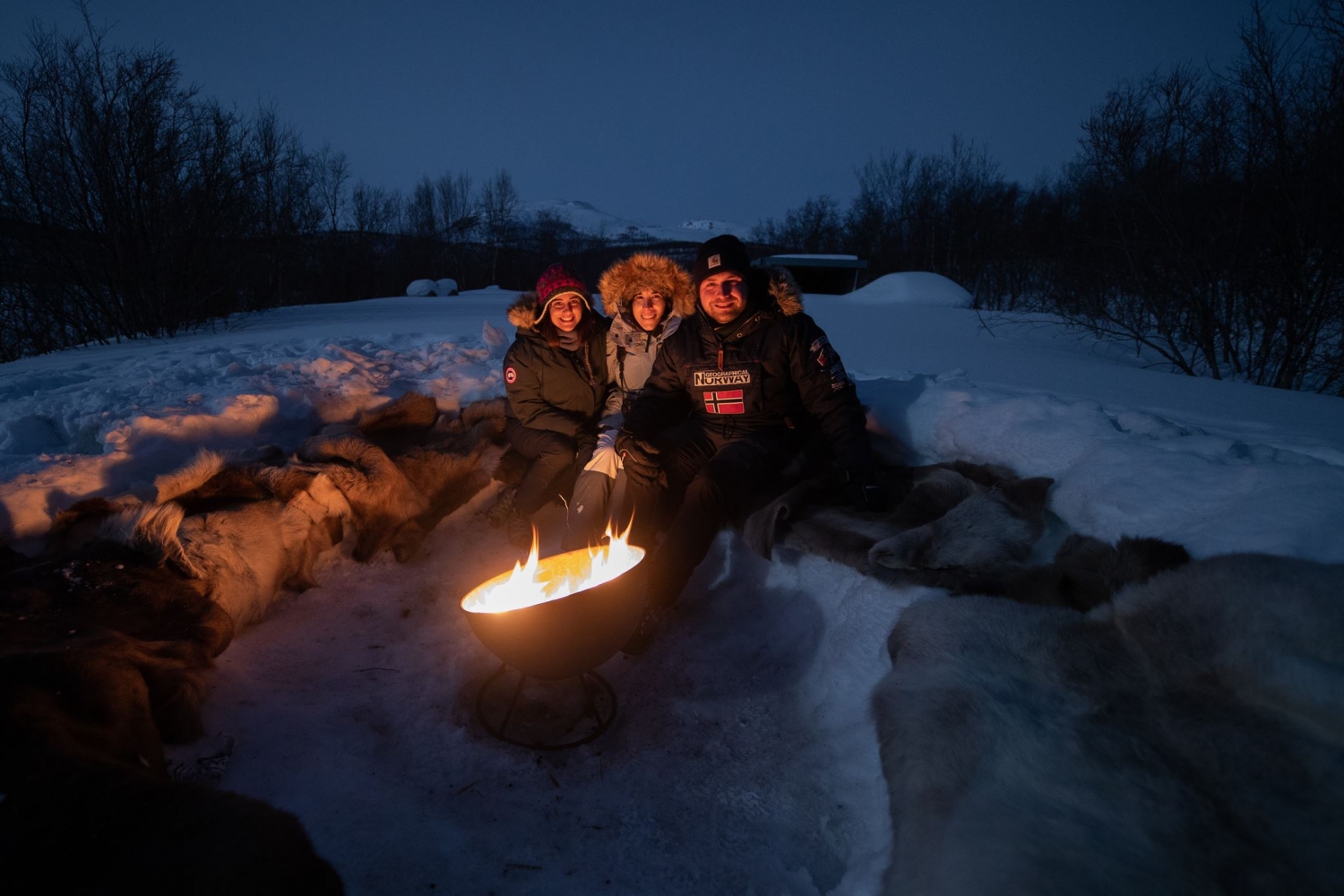 three people waiting around a bonfire