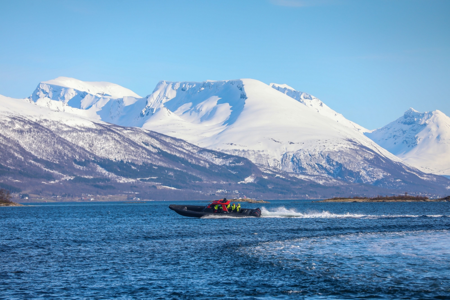 RIB båt kjører fort med snødekte fjell i bakgrunnen