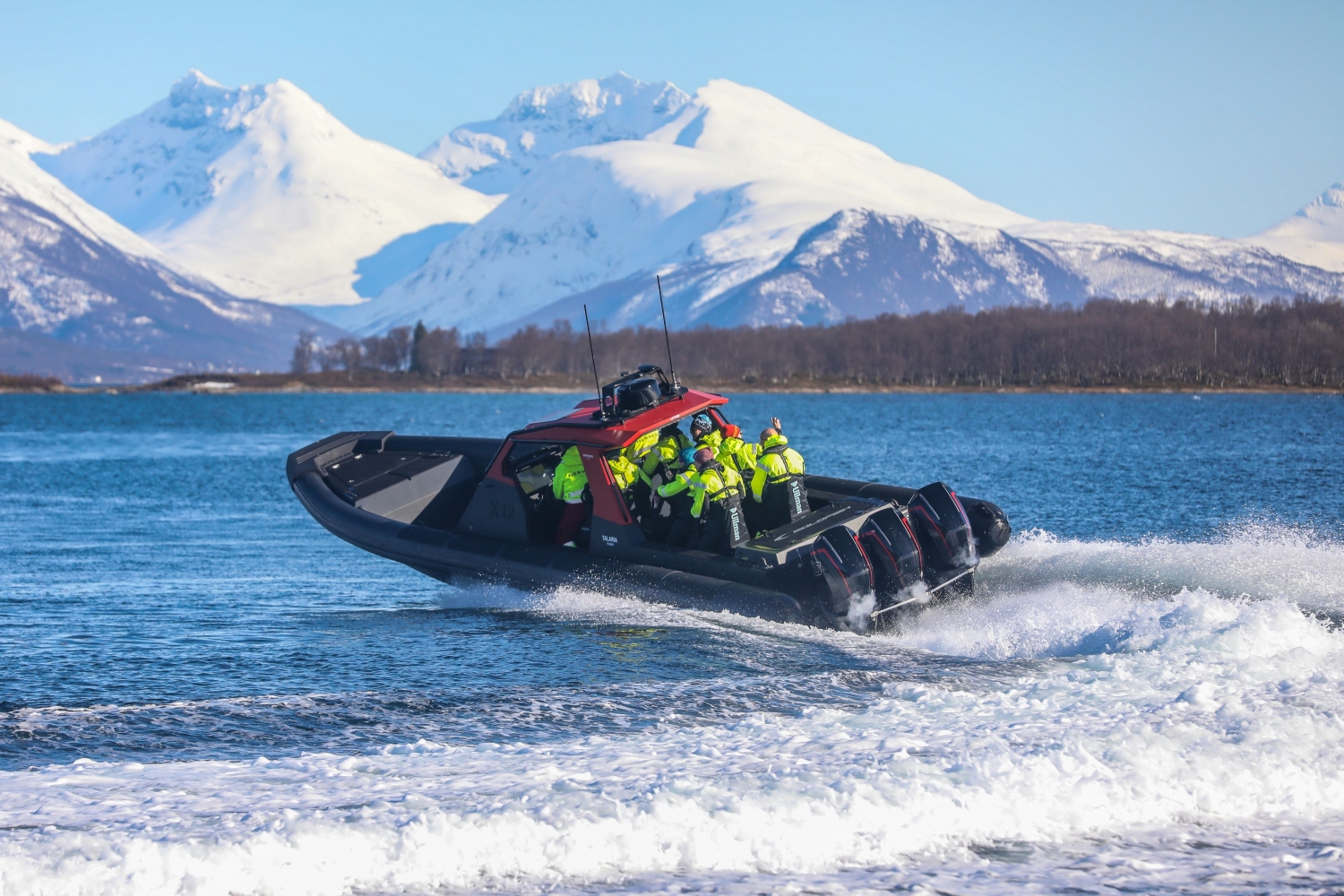 A RIB boat speeding on the water with snow covered mountains in the background