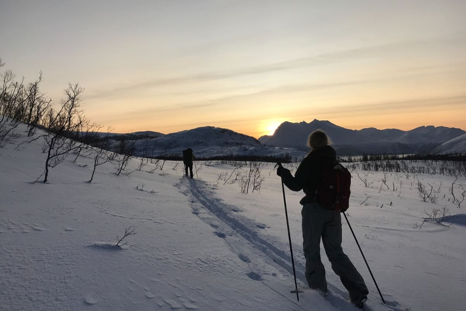 Personer går på ski mens sola går ned bakom fjellene