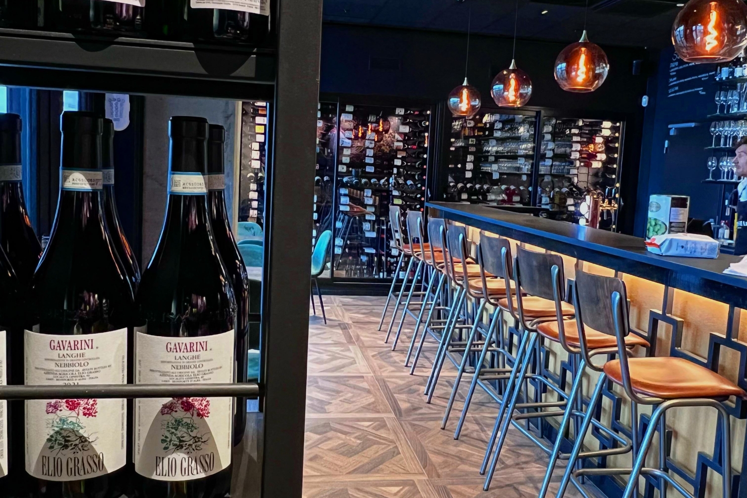 Sitteplasser ved baren, vinflasker rundt omkring i lokalet på hyller og langs veggen