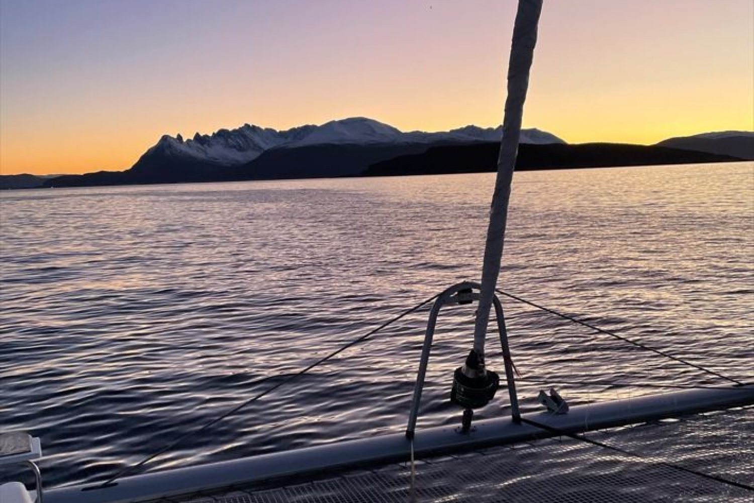 Båt ut i fjorden med fine fjell og solnedgang i bakgrunnen