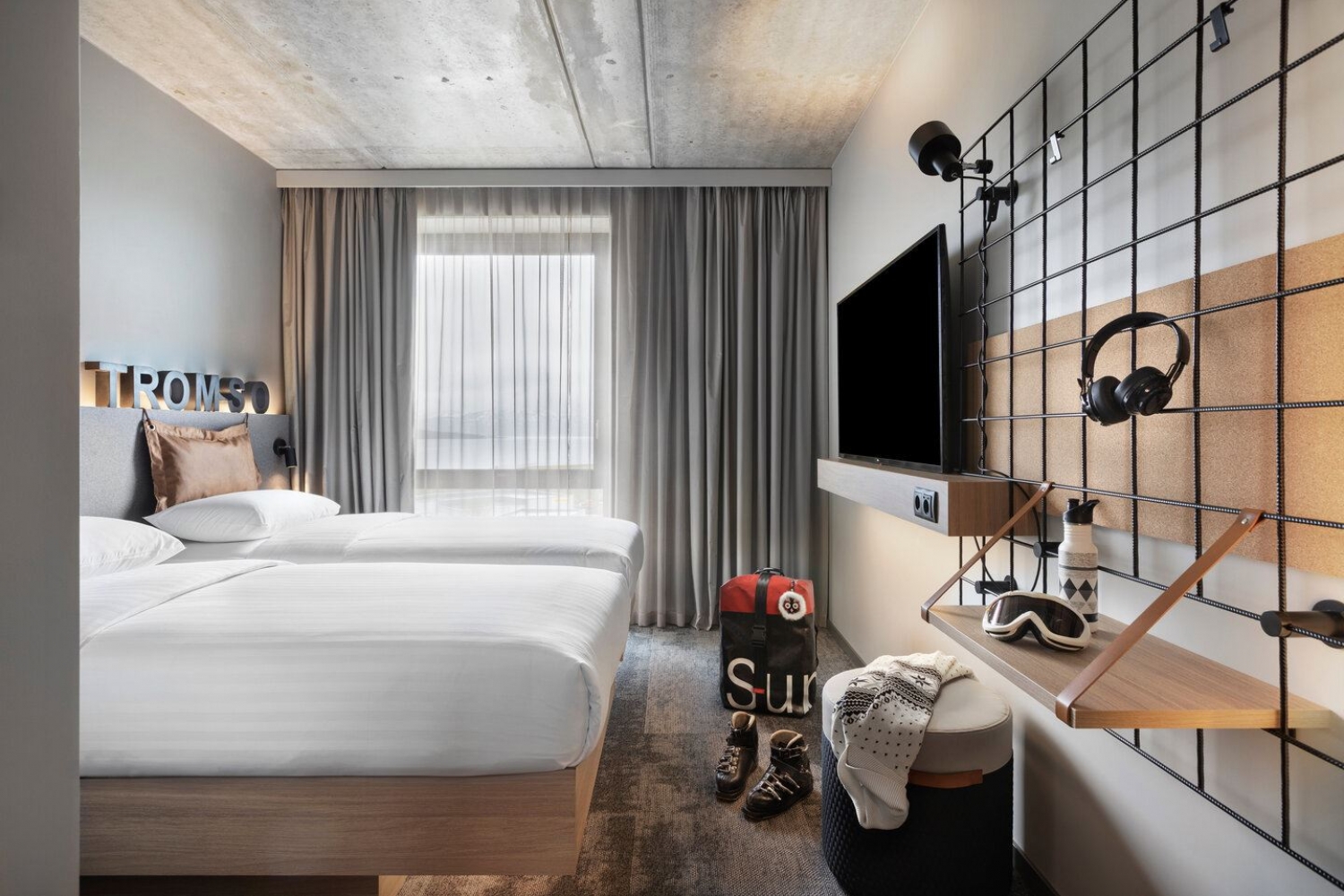 Hotellrom i minimalistisk stil, dobbeltseng, tv og hylleseksjon.