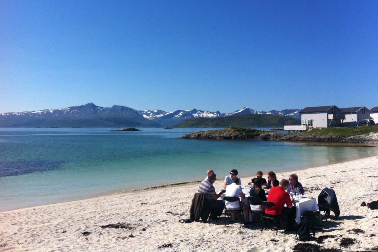 En gruppe som spiser rundt et bord på ei strand utenfor Tromsø